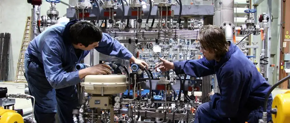 A Network Support Technician Works Behind The Curtain To Keep Things Running Efficiently 4 technicians collaborating on complex machinery in a well-organized industrial facility.