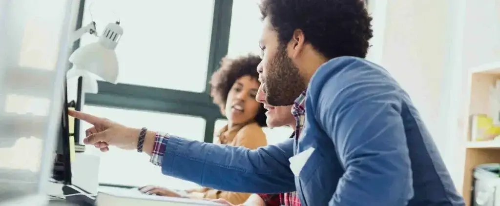 three professionals collaborate in a bright, modern office, discussing ideas around a computer.