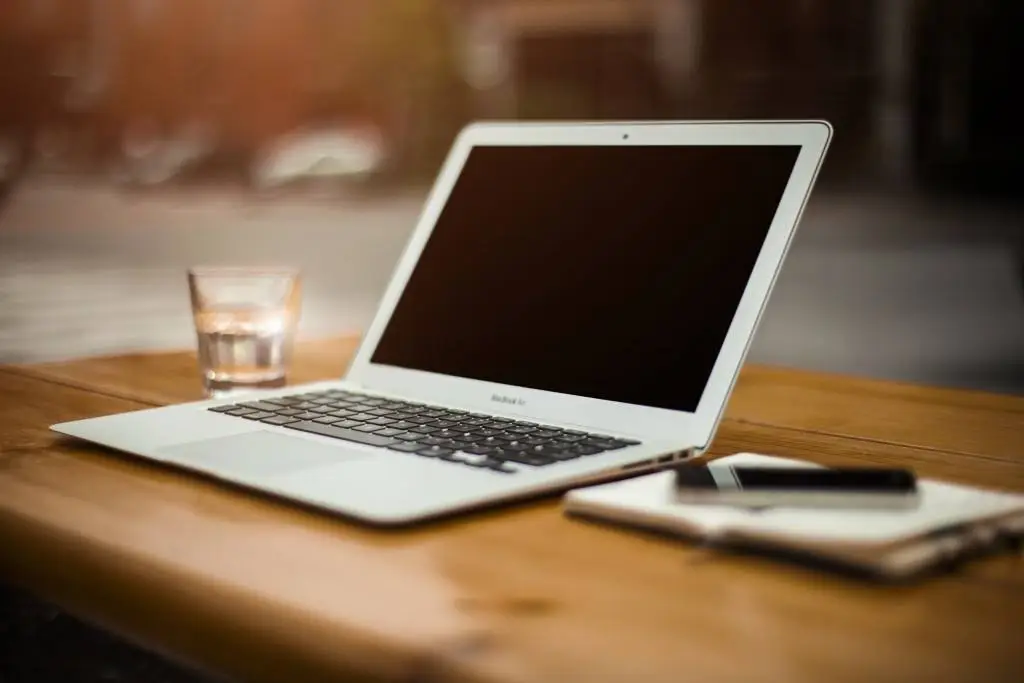 sleek laptop on wooden table, inviting creativity with water glass and notebook nearby.