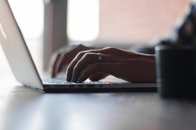 elegant hands typing on a sleek laptop in a cozy, well-lit workspace.