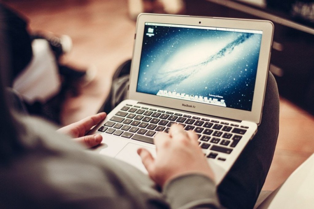 a focused individual types on a macbook air in a cozy, well-lit setting.