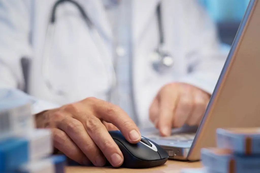 physician using laptop and mouse, symbolizing technologys role in modern healthcare practices.