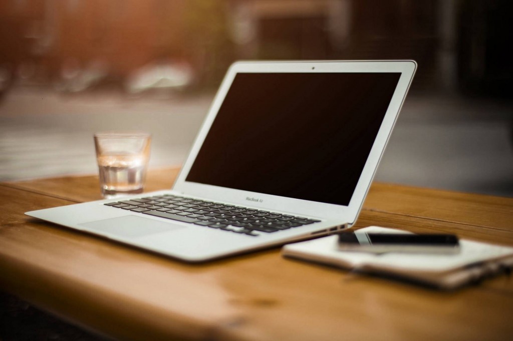 cozy minimalist workspace featuring a macbook, notebook, and glass of water for productivity.