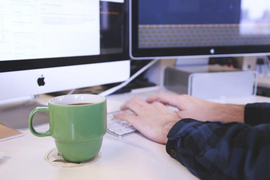 minimalist workspace featuring a keyboard, vibrant mug, and sleek monitors for productivity and comfort.