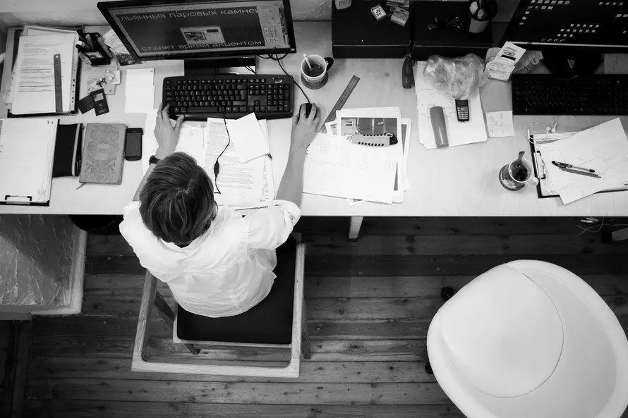 Why Do Businesses Hire Managed It Services? 8 focused professional in a busy workspace with dual monitors and cluttered desk activities.