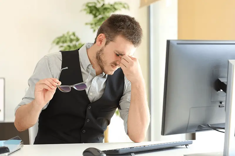 Young man stressed at desk, balancing work challenges and eye care tips in bright workspace.