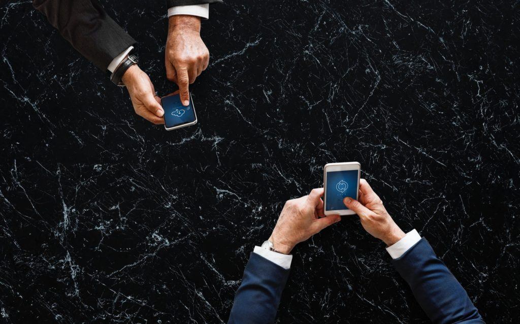 two professionals collaborate on smartphones over a sleek dark marble surface.