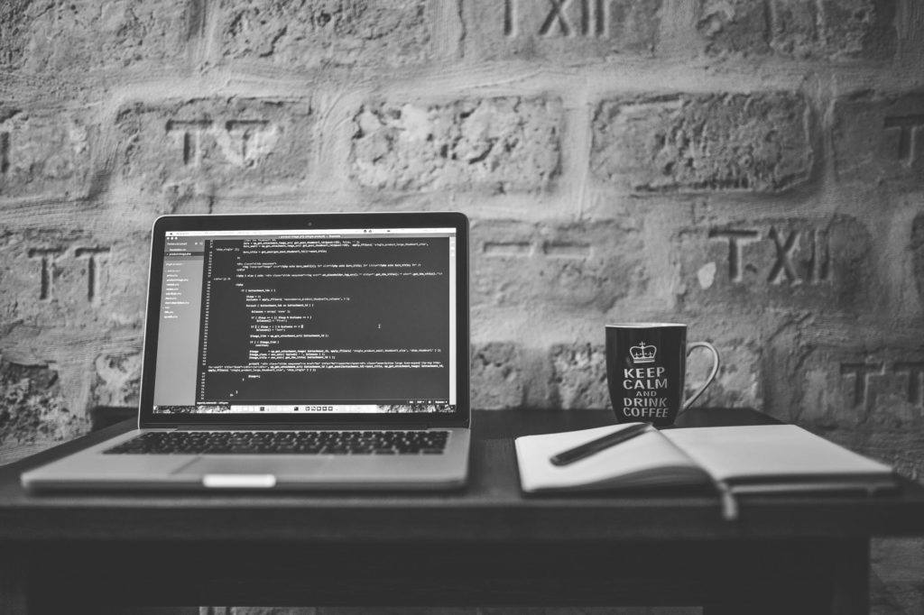 cozy workspace with laptop, notebook, and coffee mug against rustic stone wall backdrop.