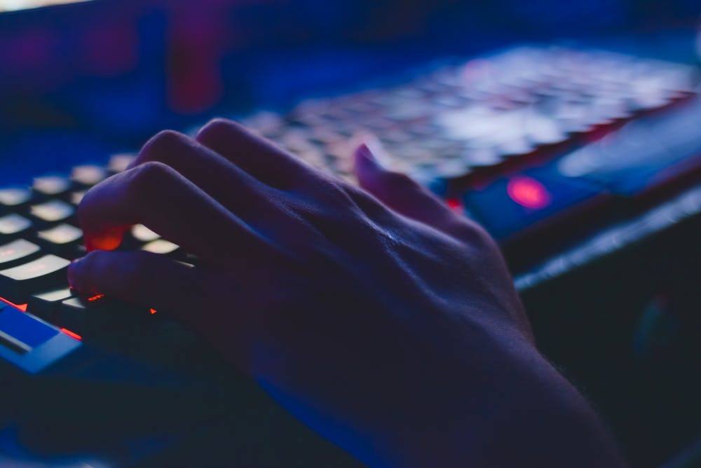 close-up of a hand typing on a backlit keyboard in a dimly lit environment.