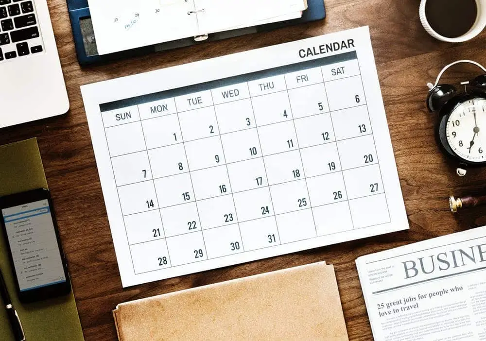 Organized workspace with a central calendar, laptop, smartphone, and traditional newspaper for productivity.