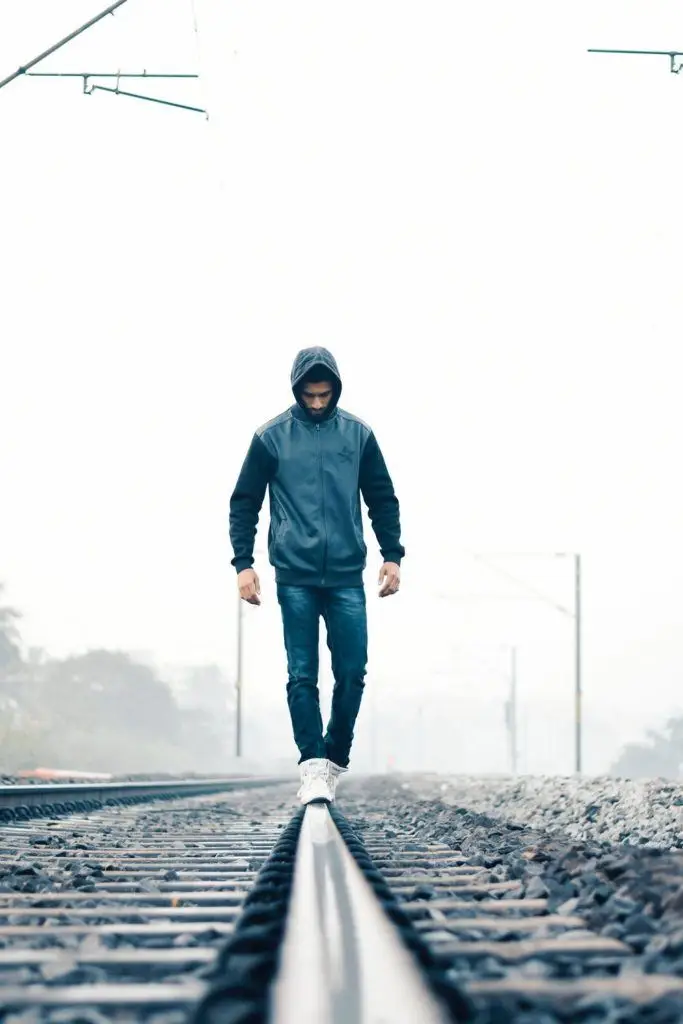 man in a hoodie walks alone on foggy railroad tracks, symbolizing introspection and solitude.