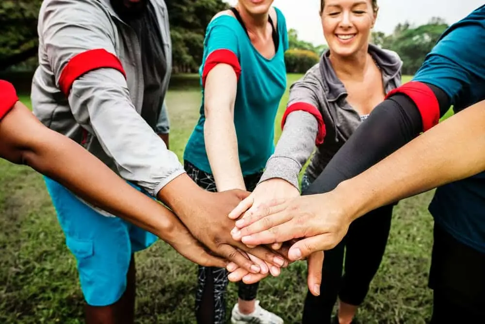 Team Collaboration Conflict? How To Successfully Collaborate Among Your Team 1 diverse team united in athletic wear, hands together, ready for an energetic outdoor activity.