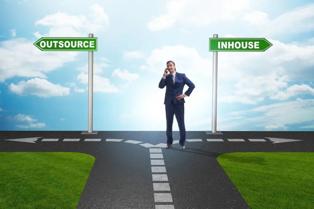 businessman at a crossroads, considering outsourcing versus in-house it support options.