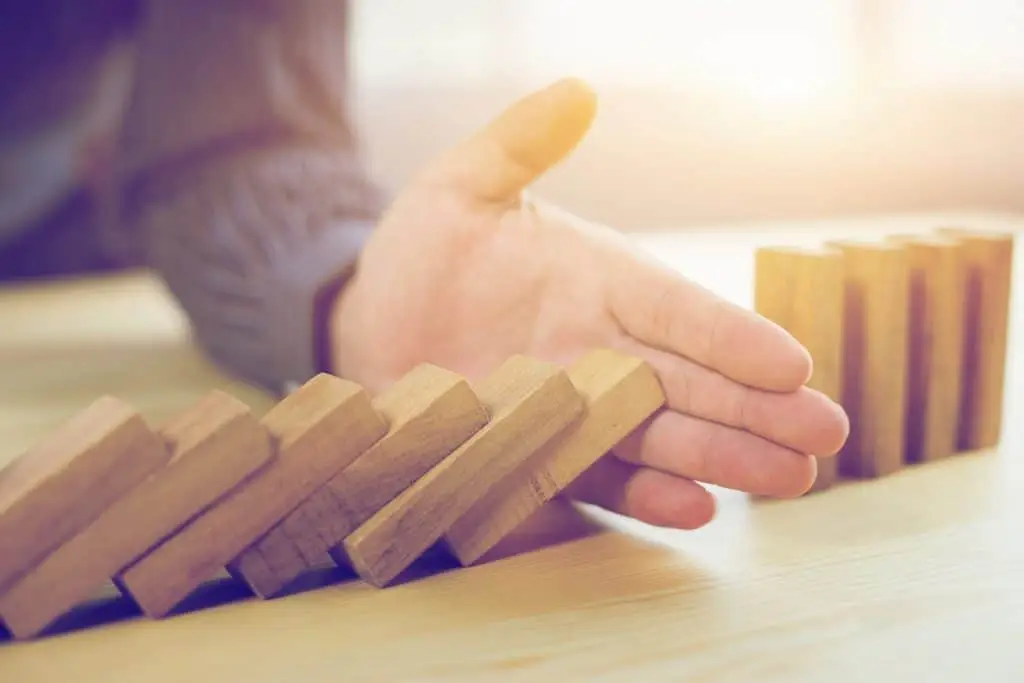 An Ounce Of Prevention Is Worth A Pound Of Cure 3 a hand stabilizes a precarious arrangement of wooden domino-like blocks on a warm table.