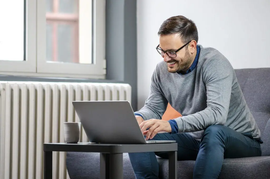 6 Cyber Security Tips For Remote Workers 6 young man in a gray sweater working on a laptop in a cozy, well-lit space.
