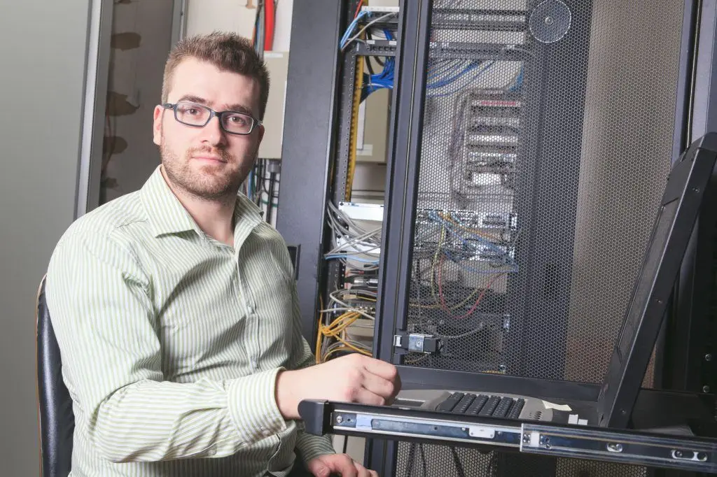 Should I Hire An It Guy Or An Msp? 5 young it specialist working on laptop in a busy server room environment.
