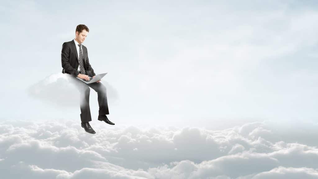 businessman working on a laptop while sitting on a fluffy cloud in a serene sky.