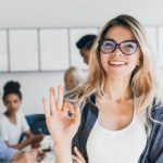 confident young woman in stylish outfit smiles amid lively collaborative workspace.
