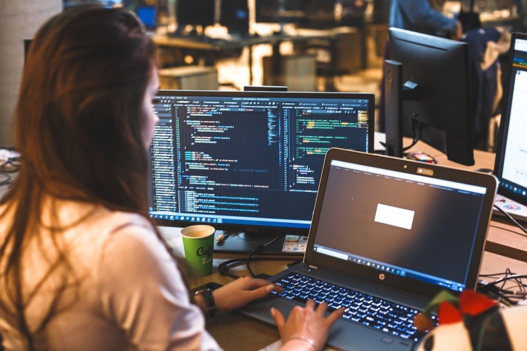 focused woman coding at a modern desk with dual laptops in a tech-inspired workspace.