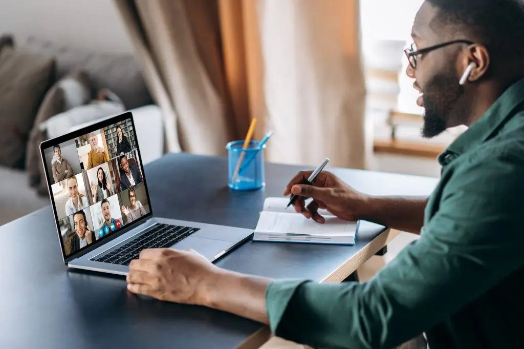 The Metric Of Productivity With Remote Work 1 focused man in a home office engaged in a virtual meeting with diverse colleagues.