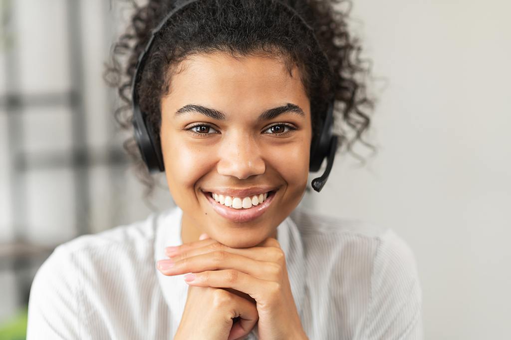 cheerful woman in headset smiles warmly, embodying modern communication in a comfortable workspace.