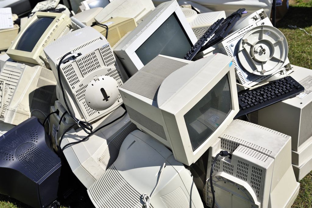 old computer monitors and keyboards discarded on grassy ground, highlighting e-waste concerns.