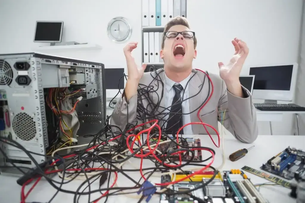 Break Your Break/Fix Cycle In 2021 1 frustrated man in a suit struggles with tangled cables in a chaotic office setting.