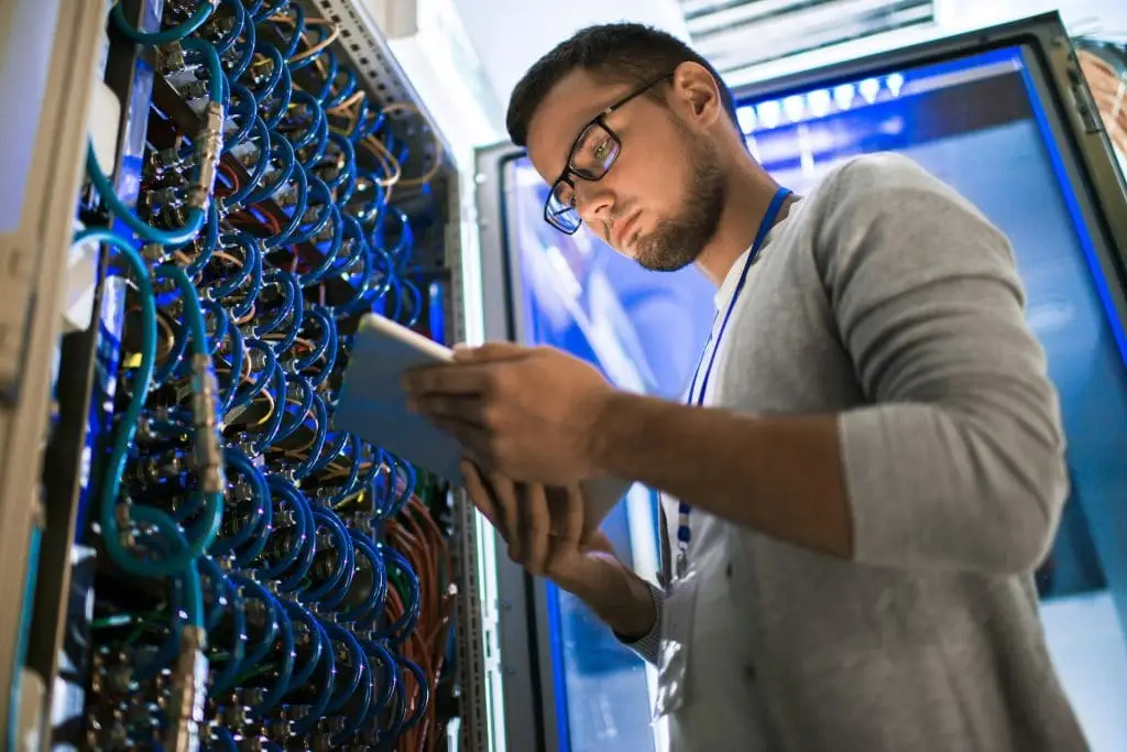 Young man with tablet focused on server rack in high-tech data center.
