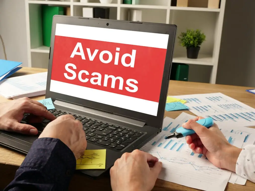 Understanding Scams: How To Protect Your Business 3 laptop with red screen warns to stay safe from online scams in a cluttered workspace.
