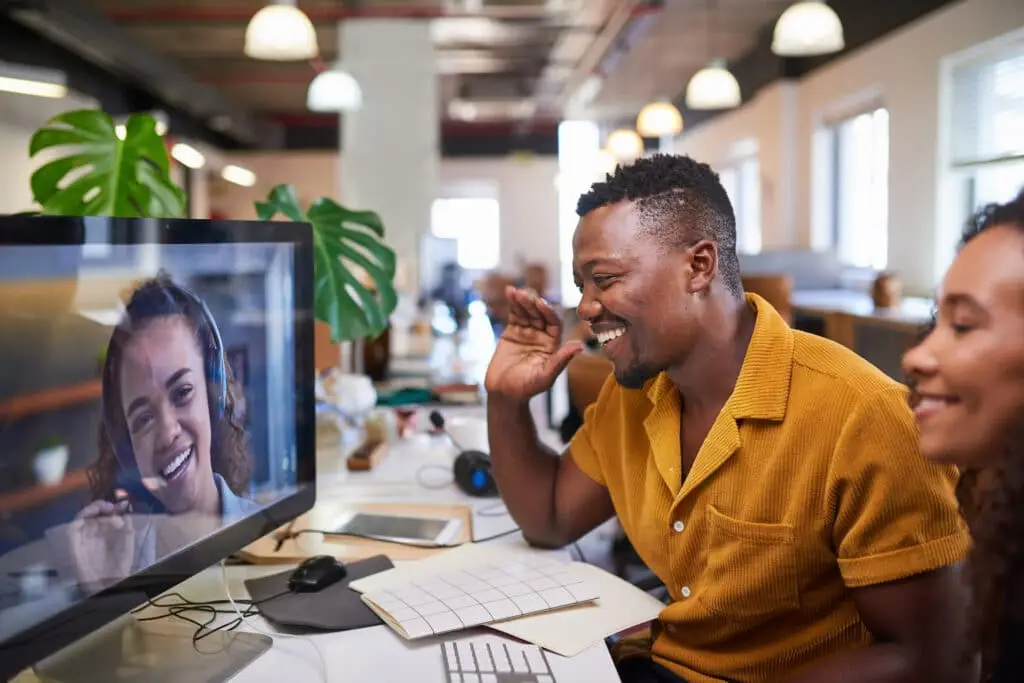 Improve Engagement In Hybrid Environments 4 a black man joyfully greets his colleague during a video call in a modern office.