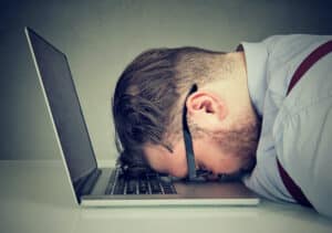 a man sleeping on his laptop with his head in his hands
