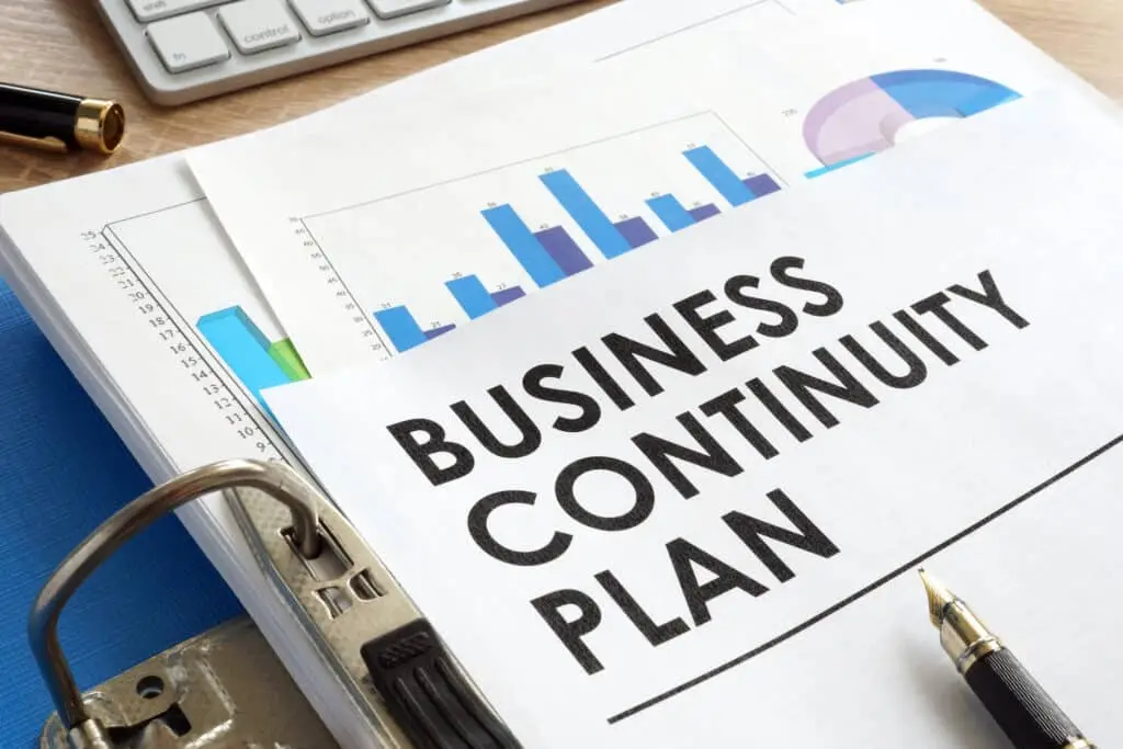 Business continuity plan document in a blue folder with charts, pen, and keyboard visible.