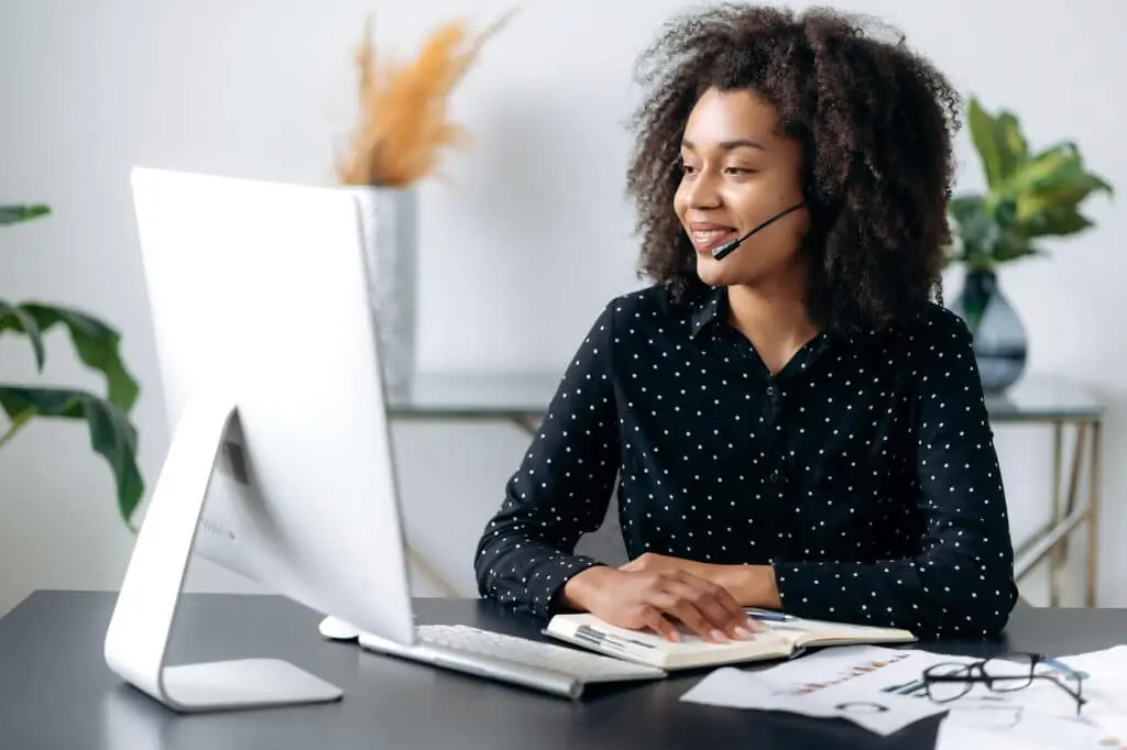 Cybersecurity Is Hard When Working Remote 4 smiling woman engaged in a virtual meeting at a stylish, organized home office desk.