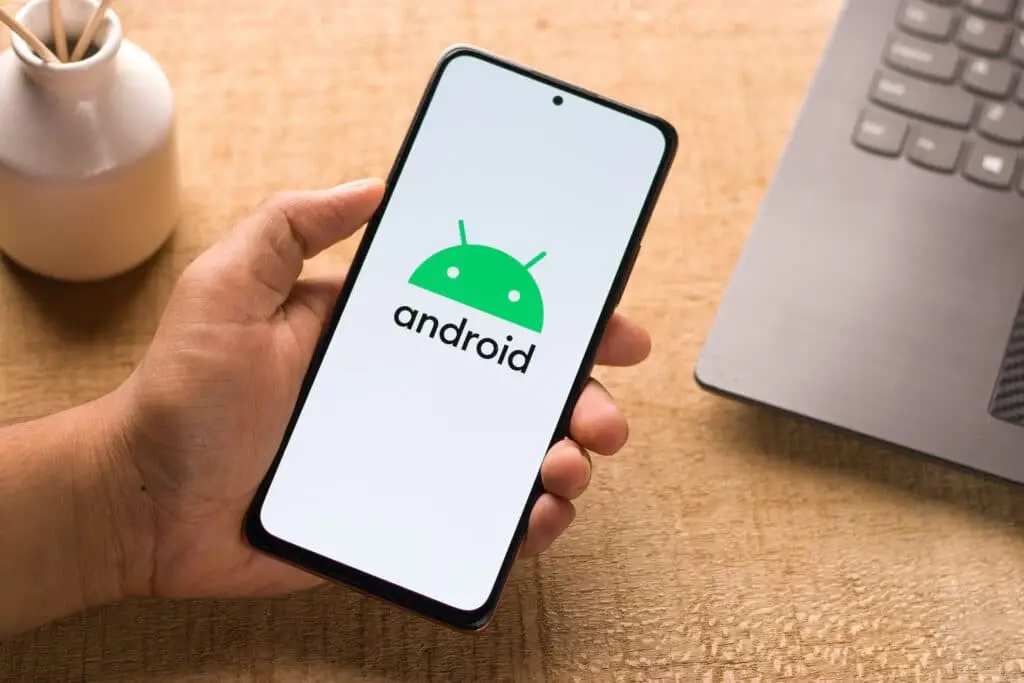 Smartphone displaying Android logo in a modern digital workspace with laptop and pen pot.