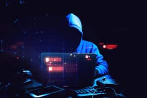 a hooded person using a laptop in the dark
