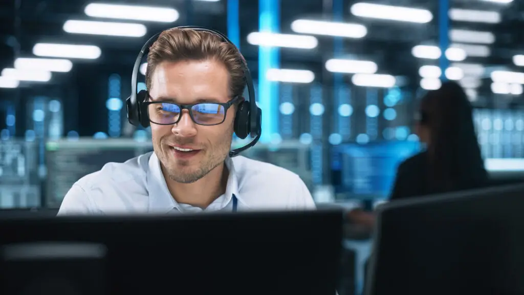 Engaged customer support specialist at modern workstation, interacting through headset and dual monitors.