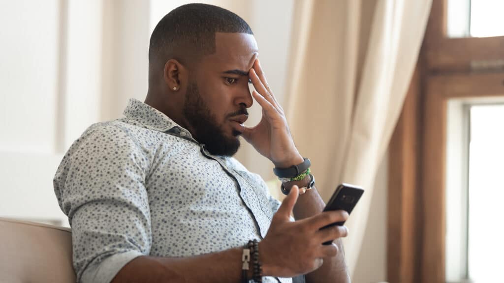 young man in distress, reflecting on his smartphone in a serene, cozy environment.