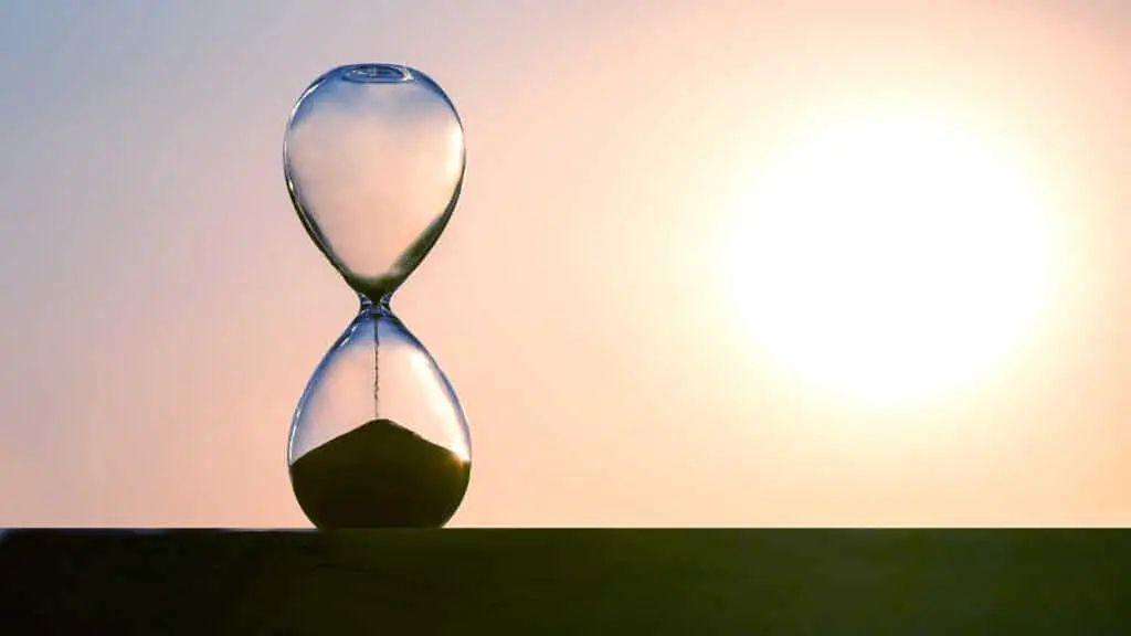 Elegant hourglass at sunset, symbolizing times passage amid vibrant sky colors.